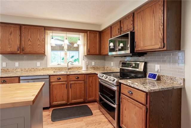 kitchen with stainless steel appliances, a sink, butcher block counters, light wood finished floors, and brown cabinetry