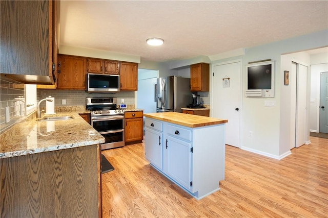 kitchen with appliances with stainless steel finishes, a sink, wooden counters, light wood-style flooring, and backsplash