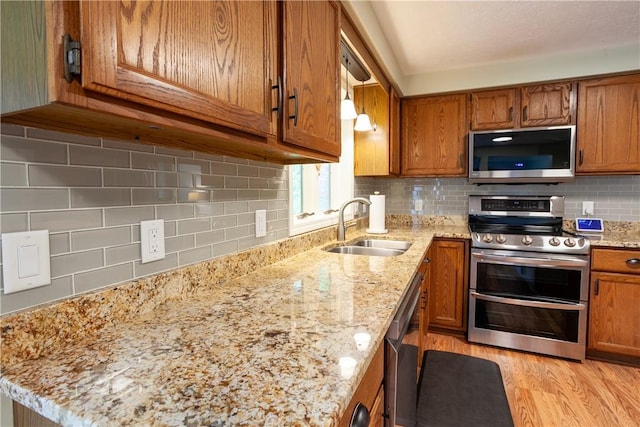 kitchen featuring appliances with stainless steel finishes, a sink, brown cabinets, backsplash, and light stone counters