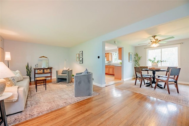 living area with light wood-style floors, baseboards, and a ceiling fan