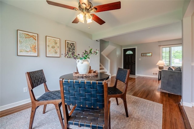 dining space featuring wood finished floors, a ceiling fan, baseboards, and stairs