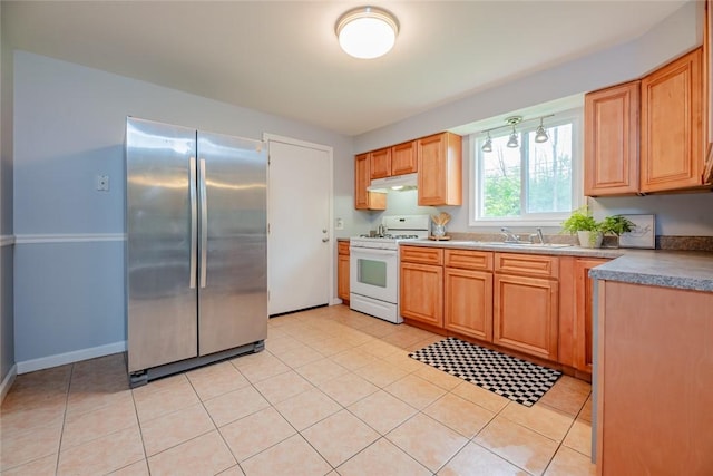 kitchen featuring freestanding refrigerator, white range with gas cooktop, under cabinet range hood, a sink, and light tile patterned floors