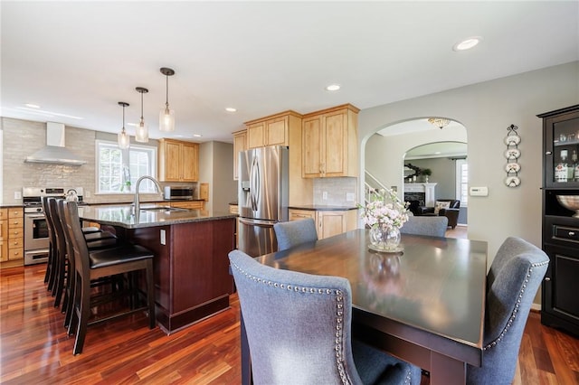 dining space with arched walkways, dark wood-style flooring, recessed lighting, and a fireplace