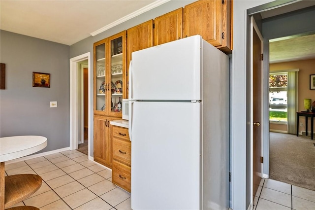 kitchen with freestanding refrigerator, light tile patterned floors, brown cabinetry, and glass insert cabinets