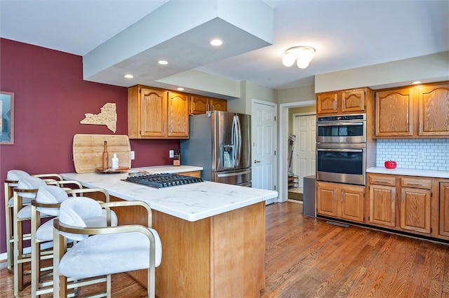 kitchen featuring appliances with stainless steel finishes, light countertops, a peninsula, a kitchen breakfast bar, and dark wood-style flooring