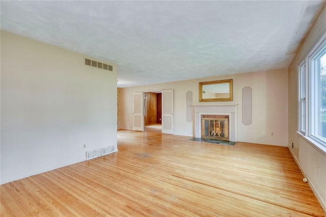 unfurnished living room with light wood-style floors, a fireplace with flush hearth, and baseboards