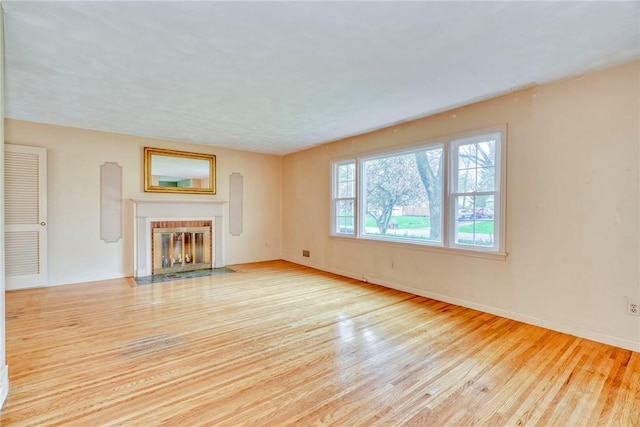 unfurnished living room with wood finished floors, a fireplace with flush hearth, and baseboards