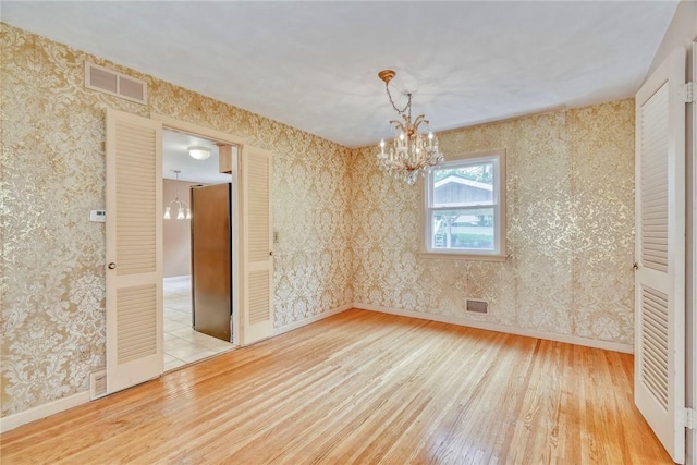 spare room featuring a chandelier, hardwood / wood-style flooring, wallpapered walls, and baseboards
