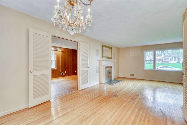 unfurnished living room with a chandelier, light wood-type flooring, baseboards, and a fireplace