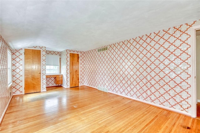 spare room with wallpapered walls, wood finished floors, baseboards, and lofted ceiling