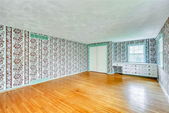 empty room with wallpapered walls, wood finished floors, and baseboards