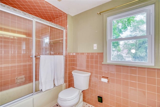 full bath with plenty of natural light, combined bath / shower with glass door, toilet, and tile walls