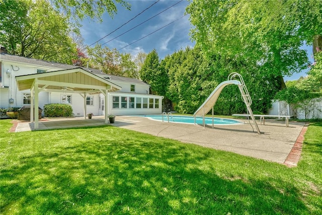 outdoor pool with a water slide, a yard, and a patio