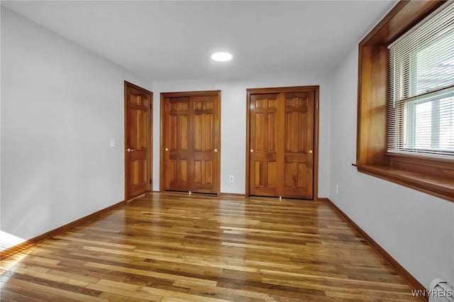 unfurnished bedroom featuring light wood-style flooring, baseboards, recessed lighting, and multiple closets