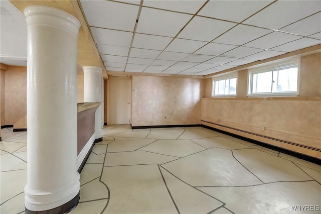 below grade area with a baseboard heating unit, a drop ceiling, baseboards, and light tile patterned floors