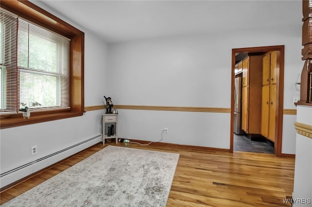 spare room with baseboard heating, light wood-style flooring, and baseboards
