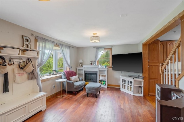 living room featuring baseboards, light wood-type flooring, a glass covered fireplace, and stairs