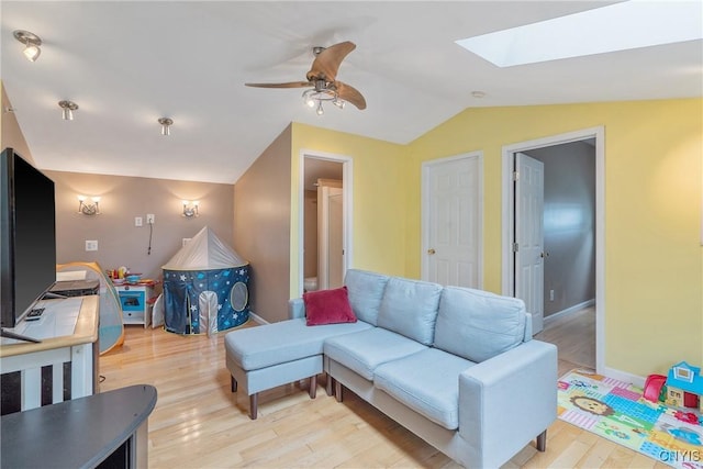 living room with vaulted ceiling, a skylight, light wood-type flooring, ceiling fan, and baseboards
