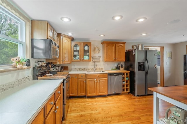 kitchen featuring stainless steel appliances, a sink, light countertops, glass insert cabinets, and light wood-style flooring