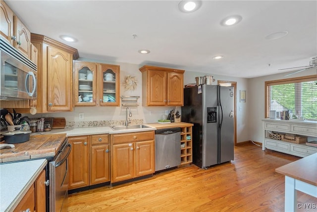 kitchen with appliances with stainless steel finishes, a sink, light wood finished floors, light countertops, and glass insert cabinets