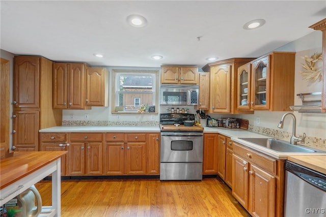 kitchen with stainless steel appliances, a sink, light countertops, glass insert cabinets, and brown cabinets