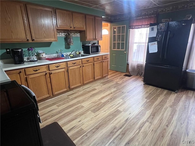 kitchen featuring freestanding refrigerator, stainless steel microwave, light wood-style floors, and light countertops