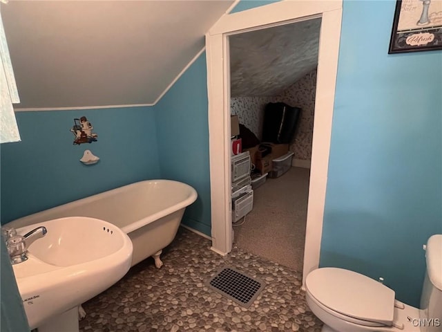 bathroom with vaulted ceiling, toilet, a soaking tub, a sink, and baseboards