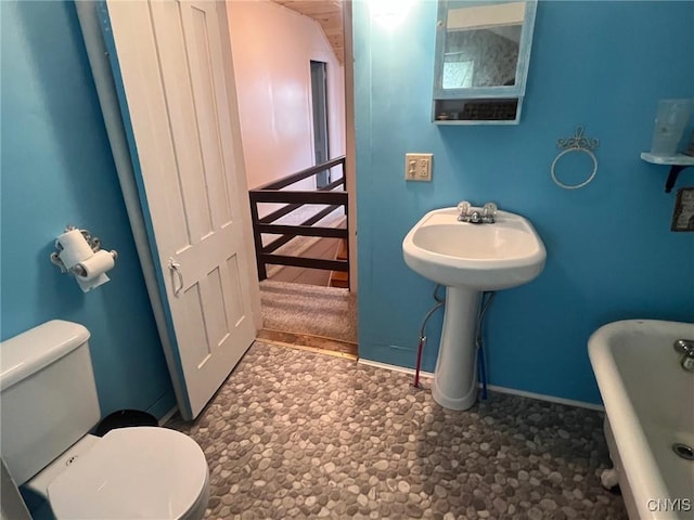 bathroom with toilet, baseboards, and a soaking tub