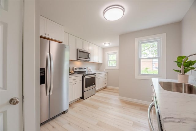 kitchen featuring appliances with stainless steel finishes, light wood finished floors, white cabinets, and baseboards