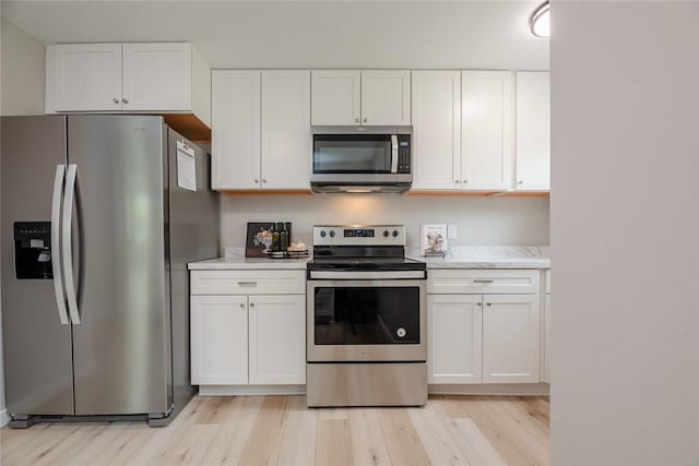 kitchen with stainless steel appliances, light countertops, white cabinetry, and light wood-type flooring