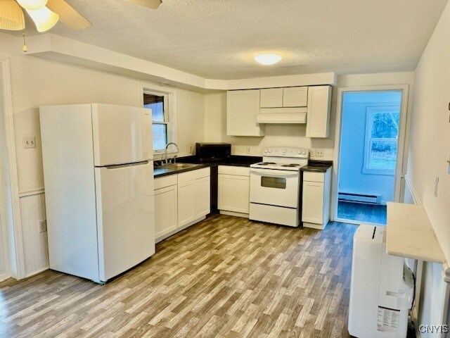 345 Orton Rd, Sandy Creek, NY 13142 - kitchen with white appliances, baseboard heating, light wood-style floors, a textured ceiling, and under cabinet range hood