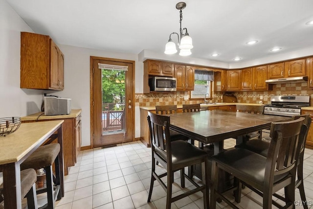 108 Pineledge Rd, Camillus, NY 13031 - kitchen featuring appliances with stainless steel finishes, under cabinet range hood, brown cabinets, backsplash, and a chandelier