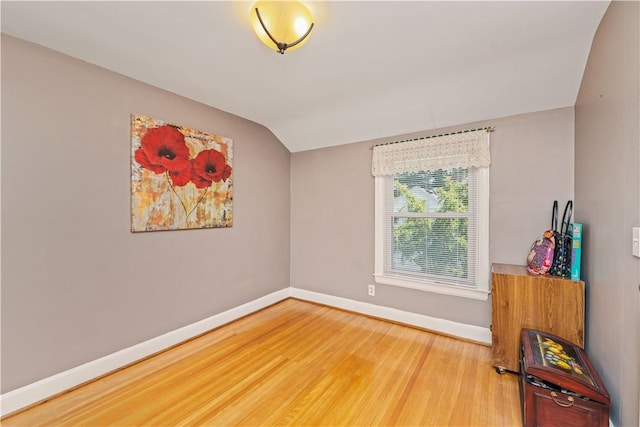 empty room featuring baseboards, wood finished floors, and lofted ceiling