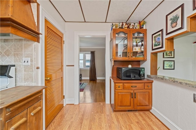 kitchen featuring black microwave, light wood-style flooring, brown cabinetry, glass insert cabinets, and decorative backsplash