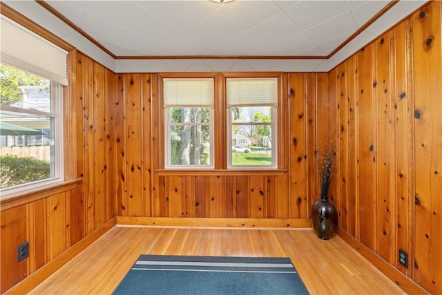 spare room featuring wood finished floors, healthy amount of natural light, crown molding, baseboards, and wood walls