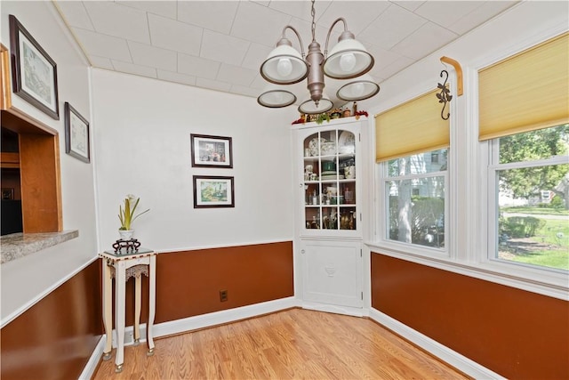 unfurnished dining area with a chandelier, light wood-type flooring, and baseboards