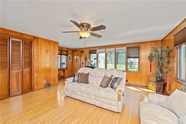 living area with healthy amount of natural light, ceiling fan, wooden walls, and light wood-style floors