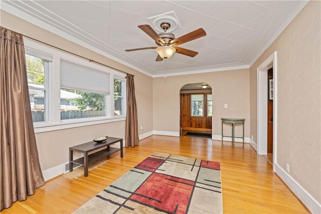 foyer entrance with arched walkways, light wood-style flooring, crown molding, a ceiling fan, and baseboards