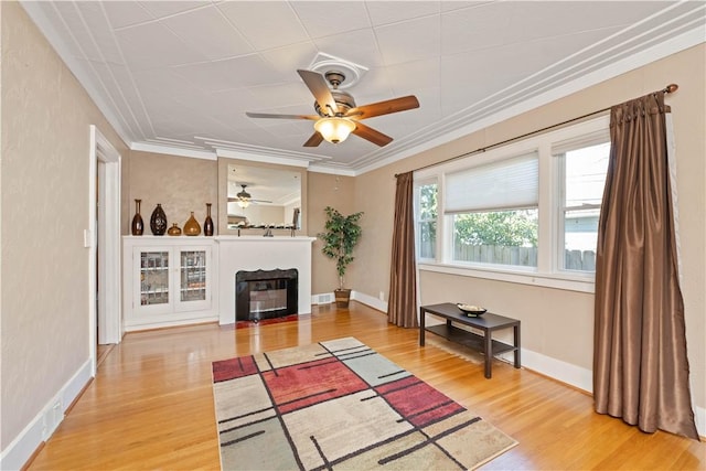 living room with ceiling fan, wood finished floors, a fireplace, ornamental molding, and baseboards