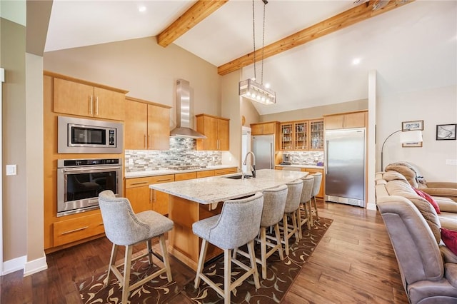 kitchen with built in appliances, wall chimney exhaust hood, open floor plan, backsplash, and a sink
