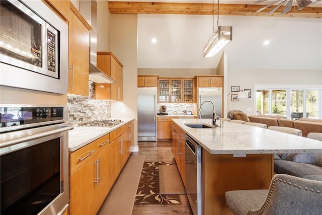 kitchen featuring built in appliances, open floor plan, a sink, beamed ceiling, and glass insert cabinets