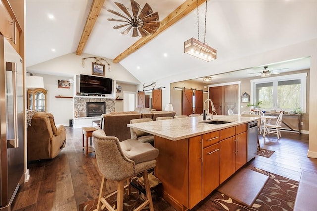 kitchen featuring stainless steel appliances, a sink, a center island with sink, dark wood finished floors, and a barn door