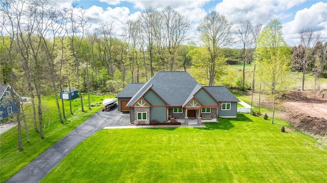 back of house featuring asphalt driveway, covered porch, a lawn, and stone siding