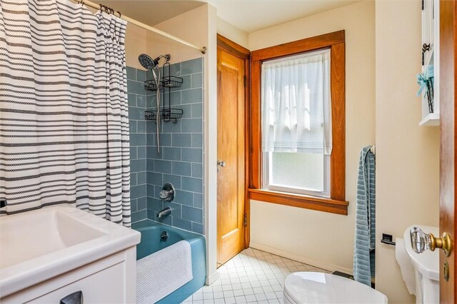 bathroom with toilet, tile patterned floors, shower / tub combo with curtain, baseboards, and a sink