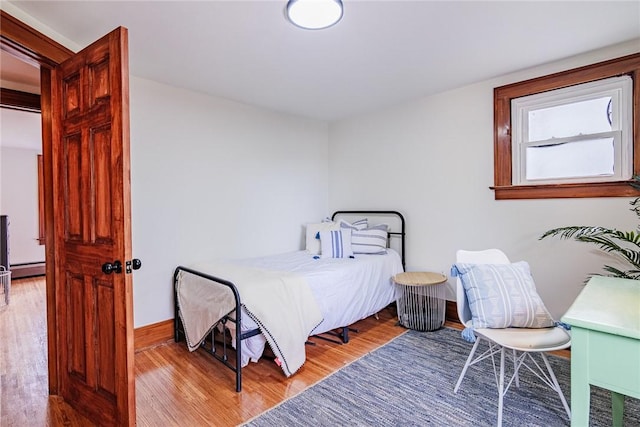 bedroom with wood finished floors, a baseboard heating unit, and baseboards