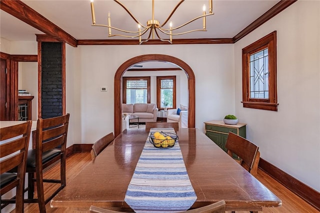 dining space with arched walkways, baseboards, wood finished floors, a chandelier, and ornamental molding