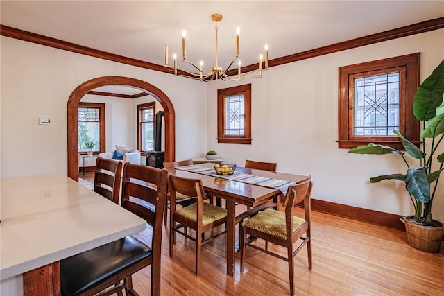 dining space featuring arched walkways, light wood-style flooring, baseboards, a chandelier, and ornamental molding