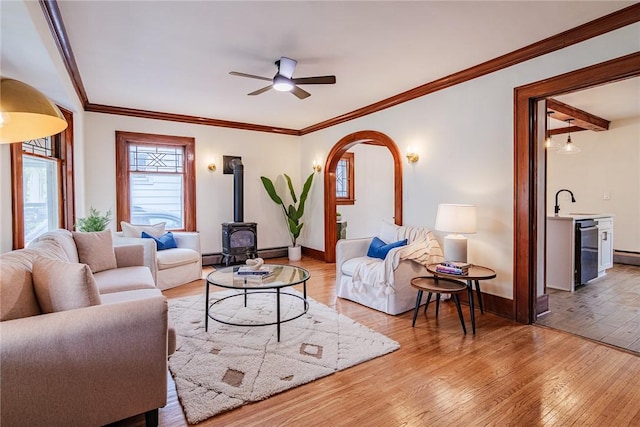 living area featuring a wood stove, light wood-style floors, baseboards, and ornamental molding