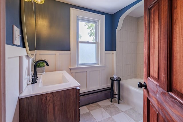 full bathroom featuring a decorative wall, a tub, wainscoting, vanity, and a baseboard radiator