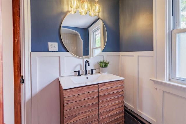 bathroom featuring a decorative wall, a chandelier, vanity, and a wainscoted wall